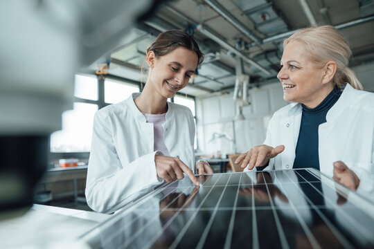 Happy scientists discussing over solar panel in laboratory - Powered by Adobe