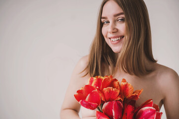 Portrait of young attractive redhead woman holds bouquet of red tulips. Minimalist light pure photo shoot. Tenderness romantic. International Women's Day