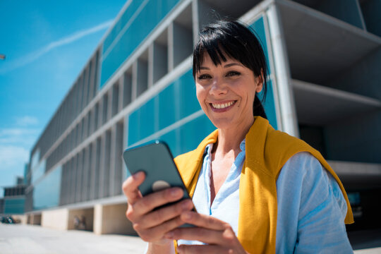 Happy mature businesswoman holding mobile phone - Powered by Adobe