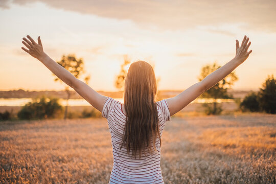 Back view of young woman watching sunset raising arms