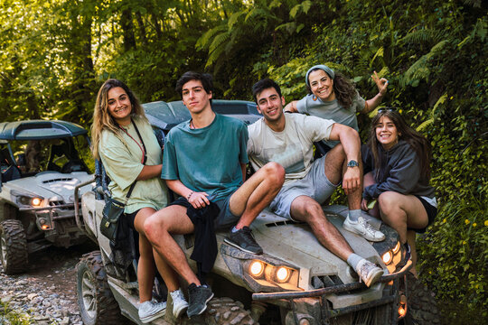 Smiling friends sitting on hood of buggy at forest