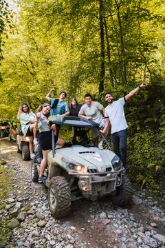 Smiling friends standing on buggy at forest