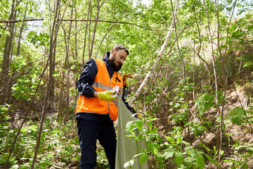 Volunteer collecting garbage amidst plants in forest