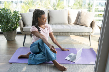 Smiling woman sitting on yoga mat with laptop at home