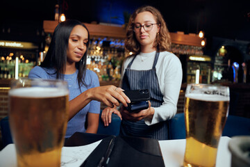 Young woman in casual clothing paying for drinks with wireless technology by waitress