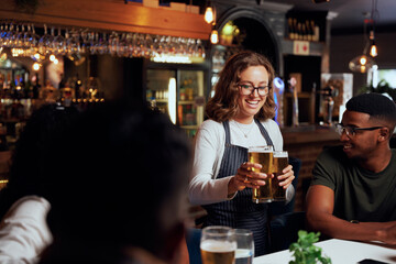 Happy young multiracial group of friends in casual clothing receiving beers from waitress at bar
