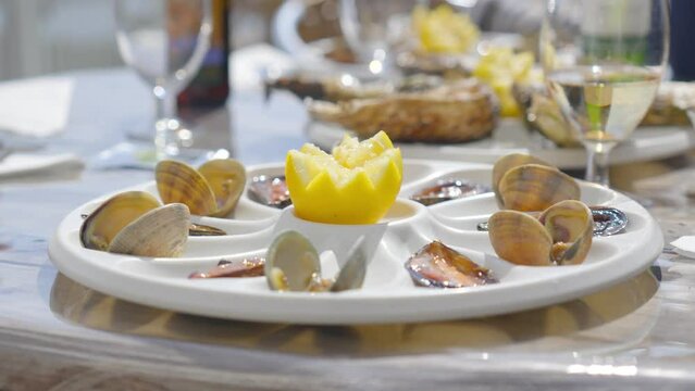 white seafood platter with half a lemon in the middle, on a light table with glasses of white wine