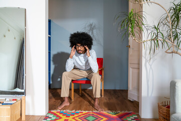 Man with hand in hair sitting on chair at home