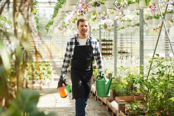 Ready for work, With watering cans. Florist man is in garden center. Successful employee is in a bright greenhouse