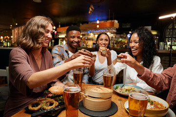 Young multiracial group of friends in casual clothing enjoying dinner and drinks at restaurant