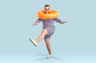 Cheerful chubby man with inflatable circle around his neck funny shows cancan dance movements on...