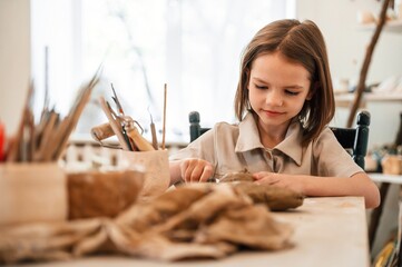 Working with clay. Little girl is learning how to do pottery in the workshop