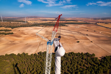 Aerial view of two professionals, attached with ropes, stand on the roof of the nacelle (hub) and install a wind turbine on a wind turbine farm, Renewable Energy, Wind Energy, Spain - obrazy, fototapety, plakaty