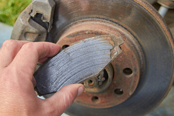 car mechanic shows a worn brake pad, a worn brake shoe and a against the background of an automobile brake disc with signs of corrosion - obrazy, fototapety, plakaty