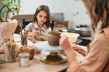Painting the product. Mother with little girl making ceramic pot at home