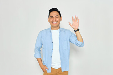 Hello. Portrait of friendly young Asian man in casual clothes showing hi gesture with waving hand...