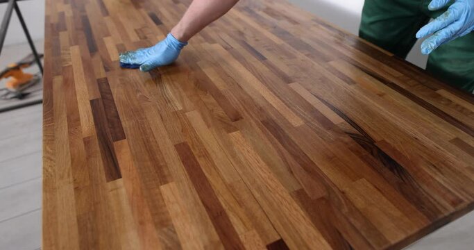 Closeup of carpenter hands in protective gloves covering wooden surface. Carpentry varnishing of piece of furniture