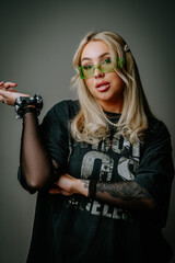 A blonde girl in green glasses and dark clothes is photographed in the studio on a dark background