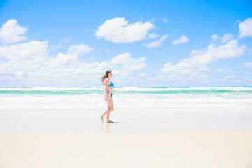 Fototapeta na wymiar 青い空と海の前を歩くビキニの白人女性