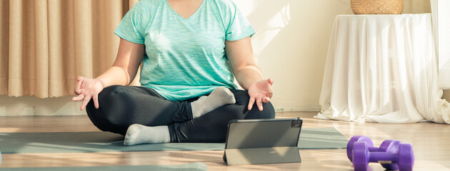 Plus size Asian woman in sport wear doing training meditation yoga at home. Healthy lifestyle and...