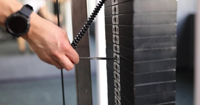 Male hand chooses weight of gym. Stack of bodybuilding equipment with metal scales in gym