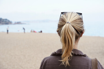 Young blonde girl with her back turned looking at the landscape with beach in the background.