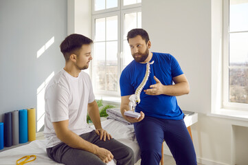 Man professional osteopath chiropractor is consulting man showing him spine layout in hospital. They talking about backbone problems. Checkup, prevention examination, diagnosis, medicine concept.