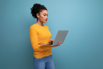 pretty smart 20s latin woman with afro hair in casual yellow sweater with laptop for study