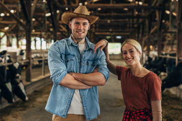 Portrait of happy young male and female farmers is a stable.