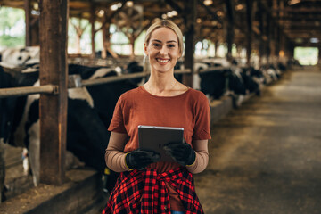 Portrait of a pretty farm girl standing in a stable with a digital tablet.