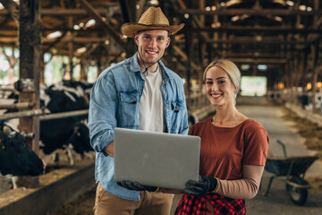 Front view of a Caucasian woman and man holding a laptop in a barn.