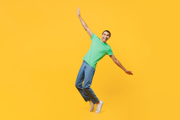 Fototapeta na wymiar Full body young man of African American ethnicity he wear casual clothes green t-shirt hat stand on toes leaning back with outstretched hands dance isolated on plain yellow background studio portrait