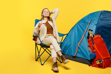 Full body young woman sit near bag with stuff tent hold credit bank card isolated on plain yellow background. Tourist leads active lifestyle walk on spare time. Hiking trek rest travel trip concept.