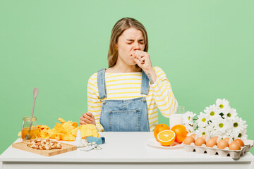 Sick unhealthy ill allergic woman has red watery eyes runny stuffy sore nose suffer from allergy trigger symptoms hay fever sit near food spread hand cough isolated on plain green background studio.