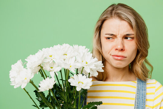 Close up sick unhealthy ill allergic sad woman has red watery eyes runny stuffy sore nose suffer from allergy trigger symptoms fever look at bouquet fowers isolated on plain green background studio.