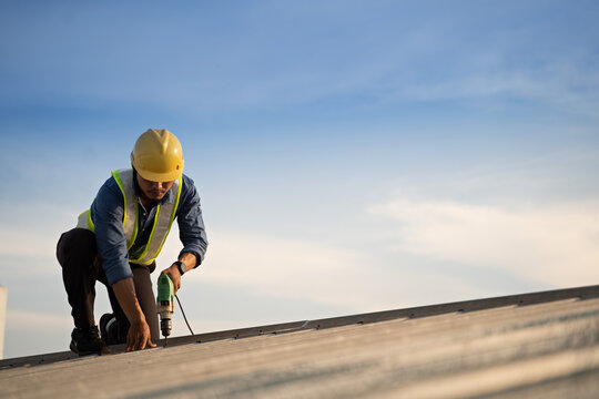 Worker repairing the roof on a construction site. Electric drill used on roof, Roof construction concept.
