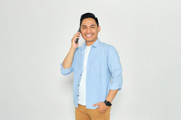 Smiling young Asian man in casual clothes talking on mobile phone and looking at camera with happy expression isolated on white background