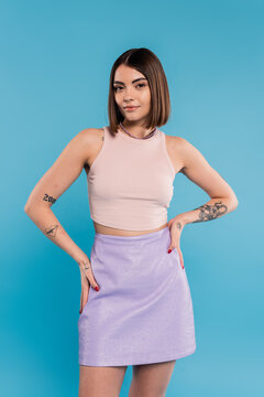 summer outfit, casual attire, happy young woman with short hair, tattoos and nose piercing standing with hands on hips on blue background, generation z, everyday style