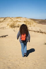 Long-haired curly-haired woman with a backpack walking on sand dunes