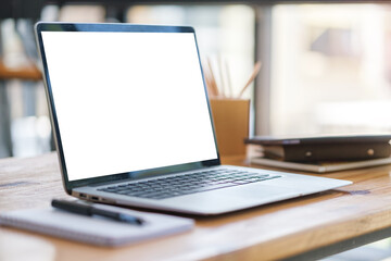 Laptop computer with white screen, notebook and pencil holder on wooden office desk.