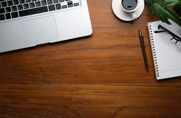 Top view of laptop computer, coffee cup, notepad and glasses on wooden working desk. Copy space for your text.