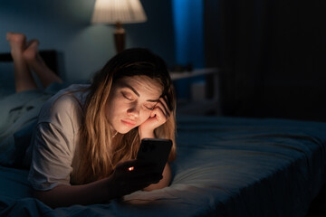 Addicted to social media young woman falling asleep with smartphone at night in bed. Mobile use...