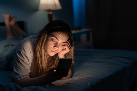 Addicted to social media young woman falling asleep with smartphone at night in bed. Mobile use addiction