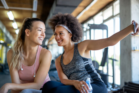 Happy fit women, friends smiling, talking and taking photos after work out in gym. Social media.