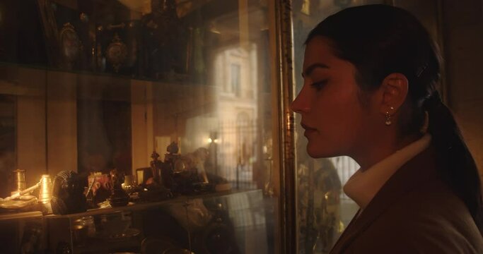 Young beautiful caucasian woman looking at ancients objects in a shop. Brunette window shopping, searching for antiques.
