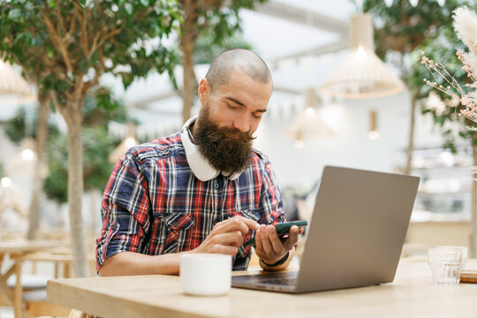 Concentrated at work. Confident young man in smart headset working on laptop in cafe drink coffee. 