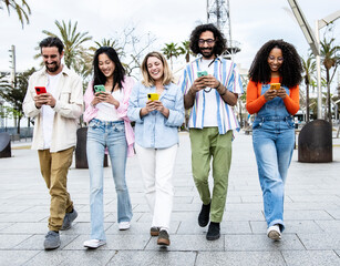 Multiethnic group of friends texting on their smartphones while walking in the street. Diverse...