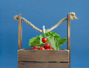 Still life of cherry tomatoes and lettuce in a wooden box on a blue background