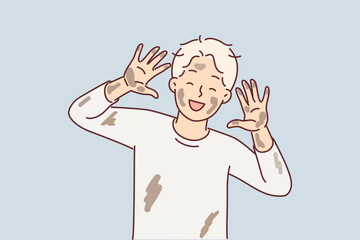 Cheerful dirty boy pre-adolescent age laughs and shows palms and face stained with clay from puddle