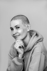 a beautiful young woman with a shaved bald head is dressed in a sweatshirt hood on a light background. Black and white photo